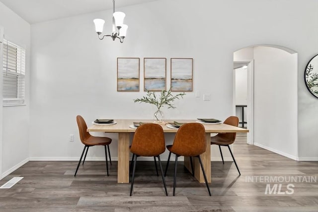 dining area featuring visible vents, baseboards, wood finished floors, arched walkways, and a notable chandelier