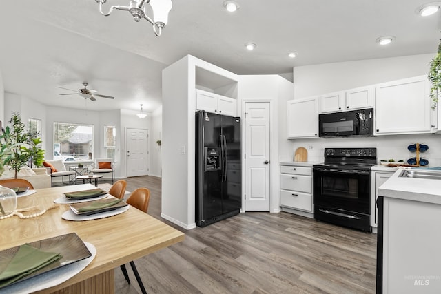 kitchen featuring light wood finished floors, black appliances, open floor plan, light countertops, and white cabinetry