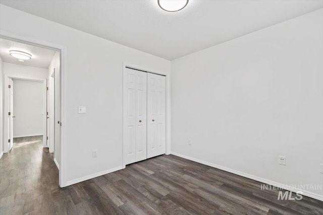 unfurnished bedroom with dark wood-style floors, a closet, and baseboards