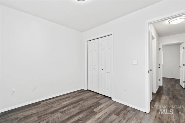 unfurnished bedroom with baseboards, dark wood-style flooring, and a closet