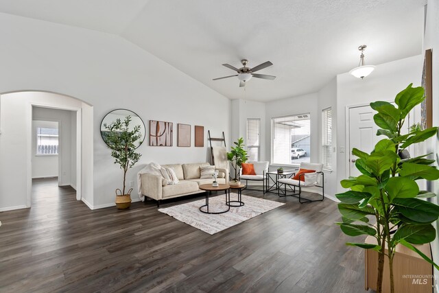 unfurnished living room featuring a wealth of natural light, arched walkways, dark wood finished floors, and vaulted ceiling