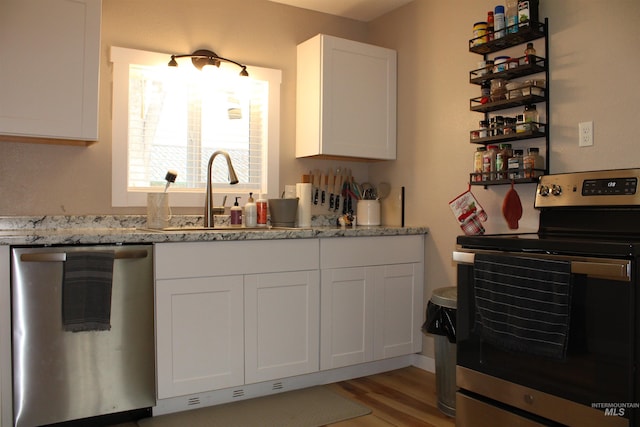 kitchen featuring white cabinetry, appliances with stainless steel finishes, light stone countertops, light hardwood / wood-style flooring, and sink