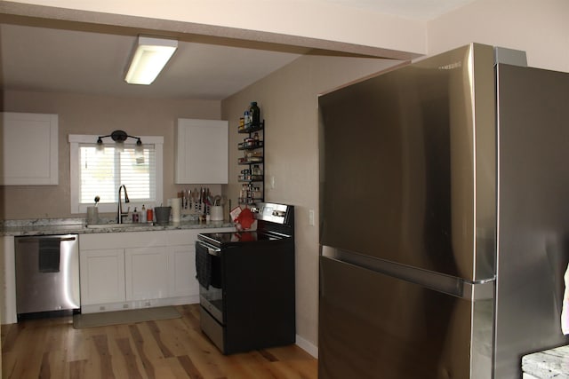 kitchen with light stone countertops, stainless steel appliances, white cabinetry, and sink