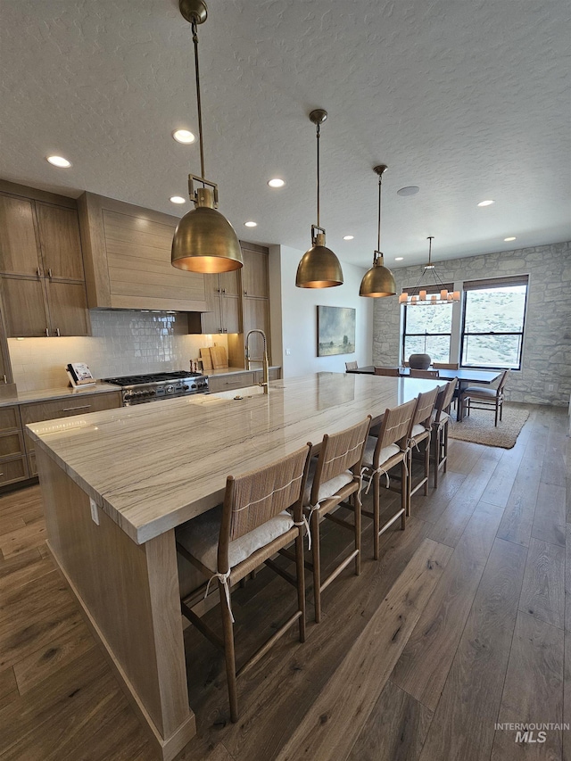 kitchen featuring dark wood-style flooring, stove, light countertops, a large island with sink, and a textured ceiling