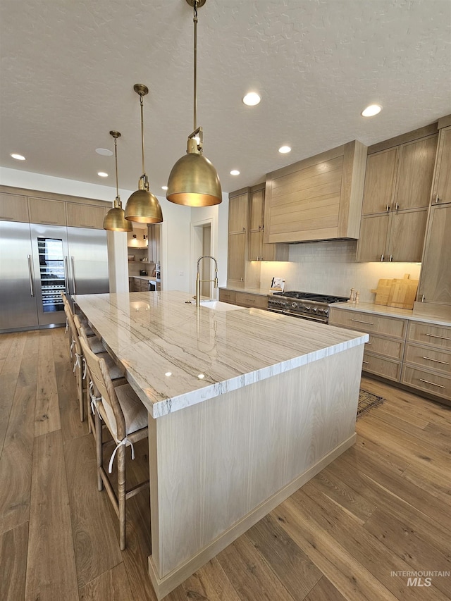 kitchen featuring recessed lighting, premium appliances, a large island, decorative backsplash, and wood-type flooring
