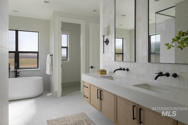 full bath featuring double vanity, decorative backsplash, a freestanding bath, and a sink