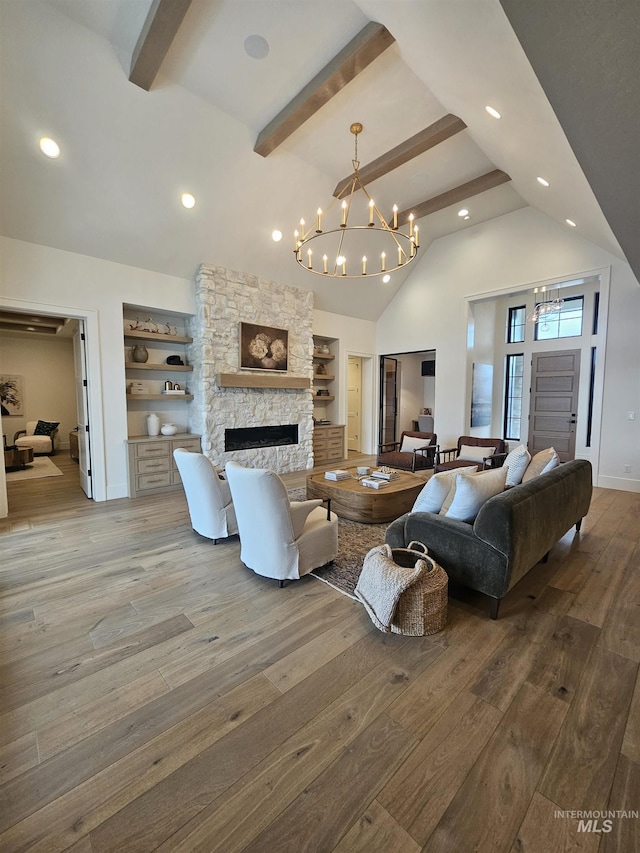 living room with wood finished floors, lofted ceiling with beams, a chandelier, and a stone fireplace