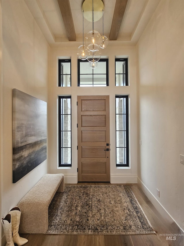 entrance foyer featuring beamed ceiling, a towering ceiling, wood finished floors, and baseboards