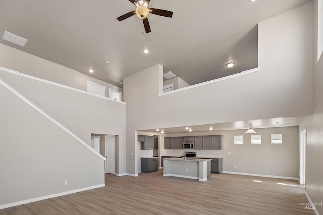 unfurnished living room featuring ceiling fan, light wood-type flooring, and a high ceiling