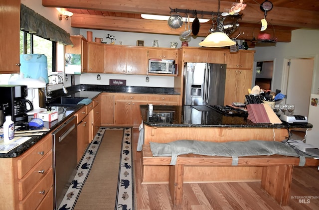 kitchen featuring stainless steel appliances, light hardwood / wood-style flooring, beamed ceiling, decorative light fixtures, and a breakfast bar area