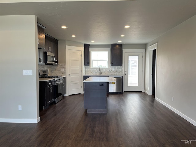 kitchen featuring stainless steel appliances, a sink, a kitchen island, light countertops, and backsplash