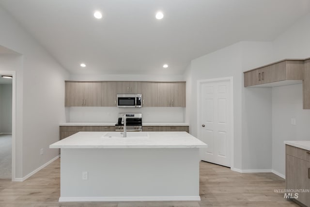 kitchen with sink, stainless steel appliances, light wood-type flooring, and an island with sink