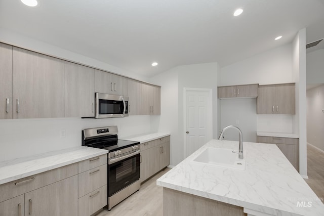 kitchen featuring light brown cabinetry, appliances with stainless steel finishes, sink, a kitchen island with sink, and lofted ceiling