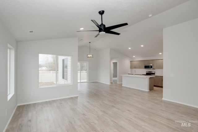 unfurnished living room featuring vaulted ceiling, ceiling fan with notable chandelier, a healthy amount of sunlight, and light hardwood / wood-style flooring