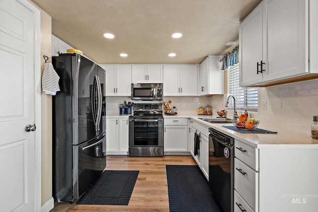 kitchen with light wood finished floors, a sink, recessed lighting, white cabinetry, and black appliances