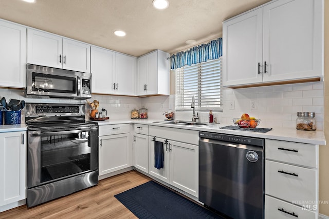kitchen with white cabinets, light wood finished floors, light countertops, a sink, and appliances with stainless steel finishes
