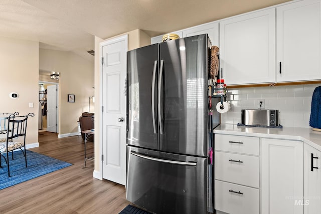kitchen featuring freestanding refrigerator, light wood-style floors, baseboards, tasteful backsplash, and white cabinetry