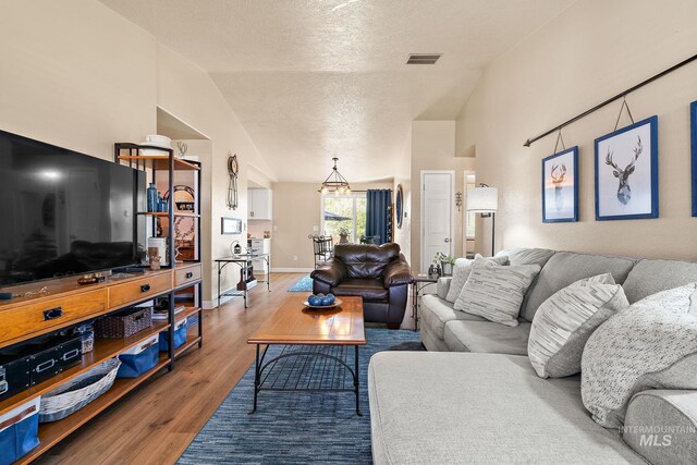 living room featuring high vaulted ceiling, wood finished floors, a textured ceiling, baseboards, and visible vents