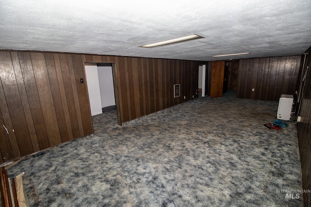 finished basement with carpet flooring, wood walls, and a textured ceiling