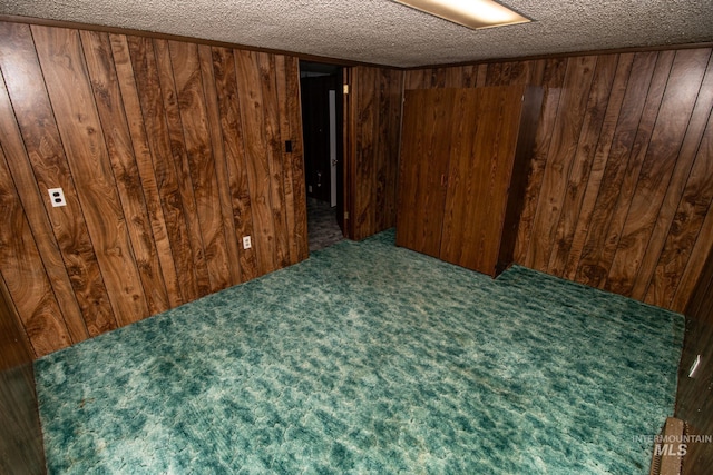 spare room featuring wooden walls, carpet flooring, and a textured ceiling