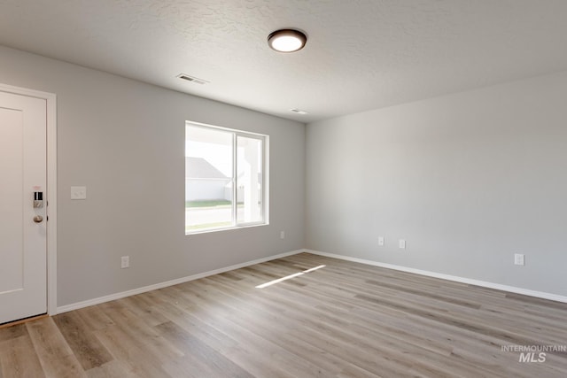 empty room with light wood-type flooring, baseboards, and a textured ceiling