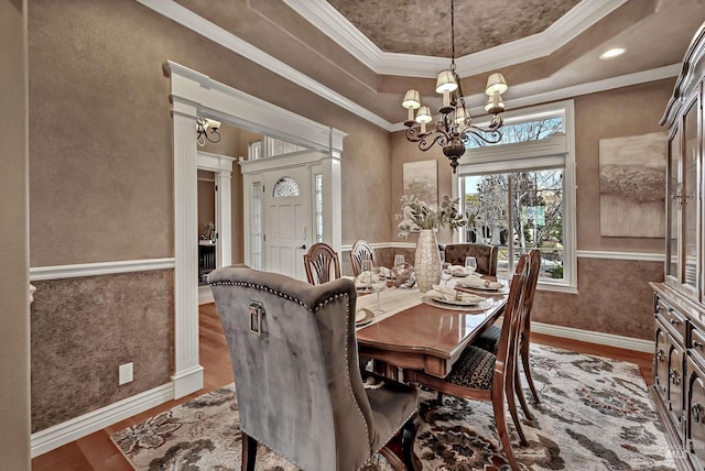 dining space with a notable chandelier, wood finished floors, baseboards, a tray ceiling, and crown molding