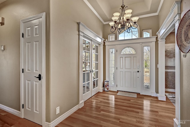 entryway with wood finished floors, baseboards, a tray ceiling, decorative columns, and an inviting chandelier