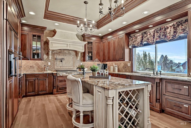 kitchen featuring an island with sink, ornamental molding, a tray ceiling, premium range hood, and a sink