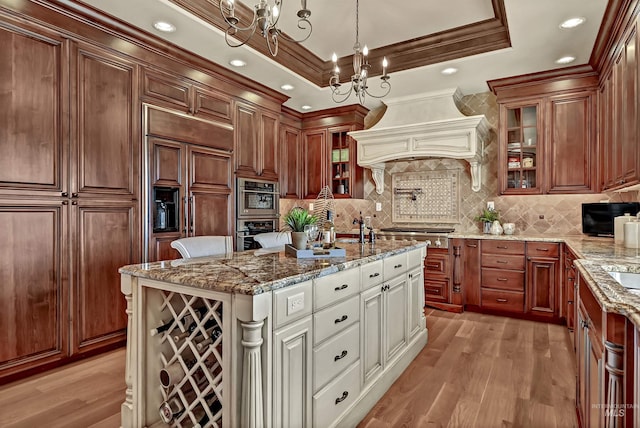 kitchen with light wood-type flooring, premium range hood, a tray ceiling, and glass insert cabinets