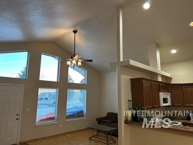 kitchen with ceiling fan, high vaulted ceiling, and stone countertops