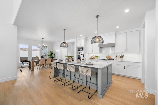 kitchen with white cabinetry, appliances with stainless steel finishes, light hardwood / wood-style floors, and a kitchen island with sink