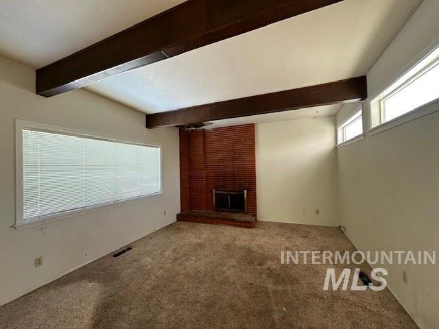 unfurnished living room featuring beam ceiling, a fireplace, and carpet flooring