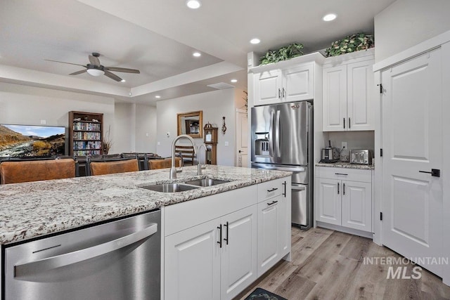 kitchen with sink, appliances with stainless steel finishes, white cabinetry, light hardwood / wood-style floors, and a raised ceiling