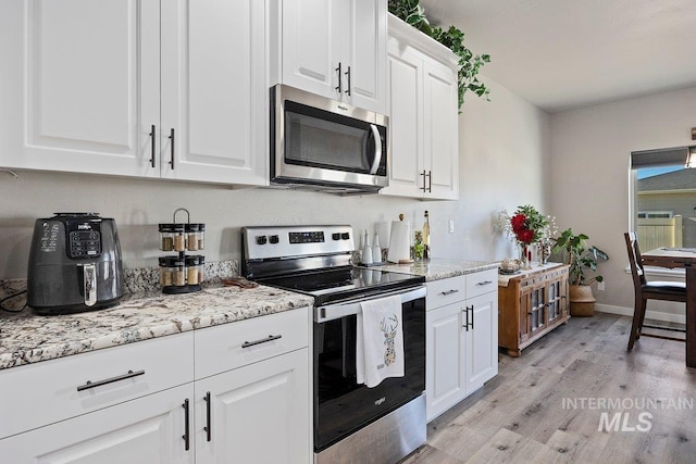 kitchen with appliances with stainless steel finishes, light stone counters, white cabinets, and light hardwood / wood-style floors