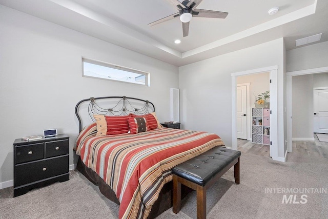 bedroom featuring ceiling fan, a tray ceiling, and light carpet