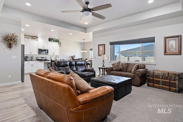 living room with a tray ceiling, light hardwood / wood-style flooring, and ceiling fan