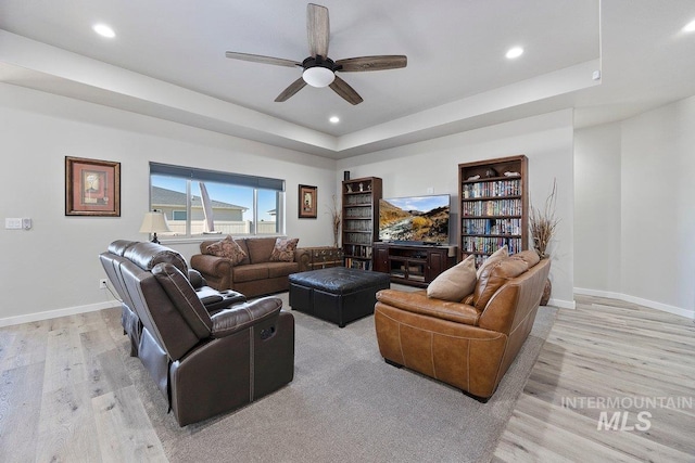 living room with a raised ceiling, ceiling fan, light wood-type flooring, and built in shelves