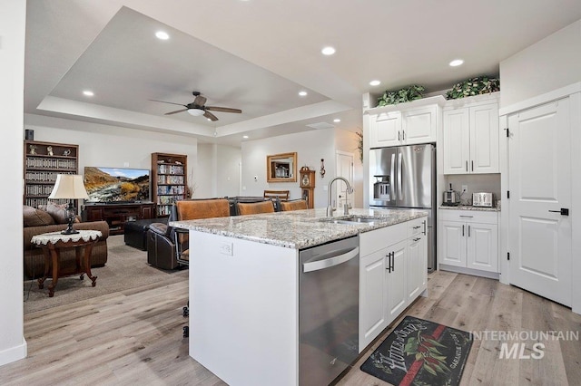 kitchen featuring sink, white cabinetry, stainless steel appliances, a tray ceiling, and an island with sink