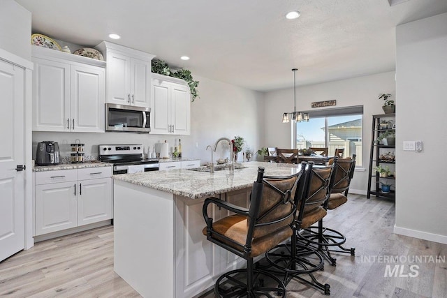 kitchen with sink, a kitchen island with sink, stainless steel appliances, light stone countertops, and white cabinets