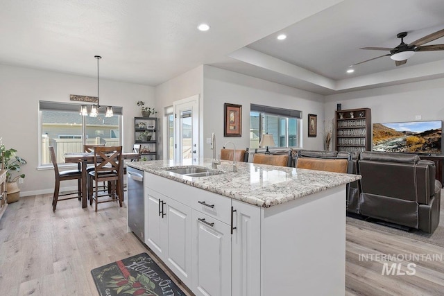 kitchen featuring sink, white cabinetry, light stone counters, hanging light fixtures, and a center island with sink