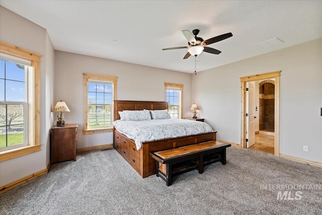 bedroom featuring light colored carpet, a ceiling fan, baseboards, and ensuite bathroom