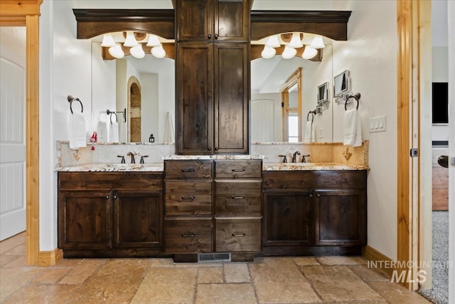 bathroom with stone tile floors, backsplash, a sink, and double vanity