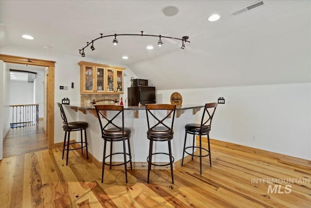 kitchen with a kitchen bar, visible vents, light wood-type flooring, freestanding refrigerator, and lofted ceiling