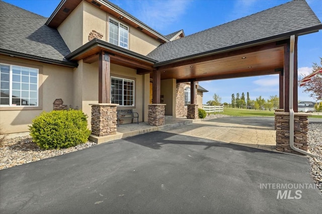 property entrance featuring a shingled roof, stucco siding, stone siding, and aphalt driveway