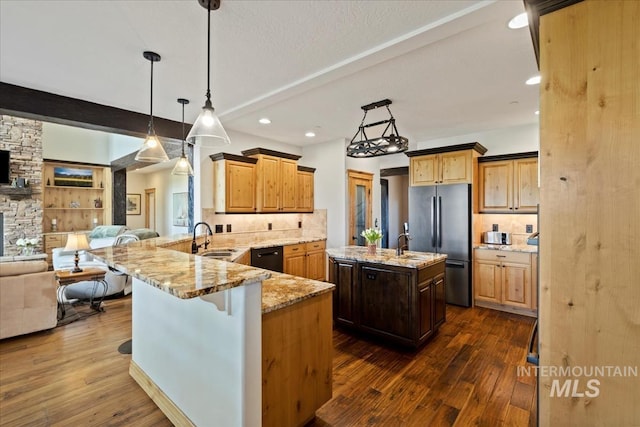 kitchen featuring freestanding refrigerator, a peninsula, open floor plan, light stone counters, and a sink