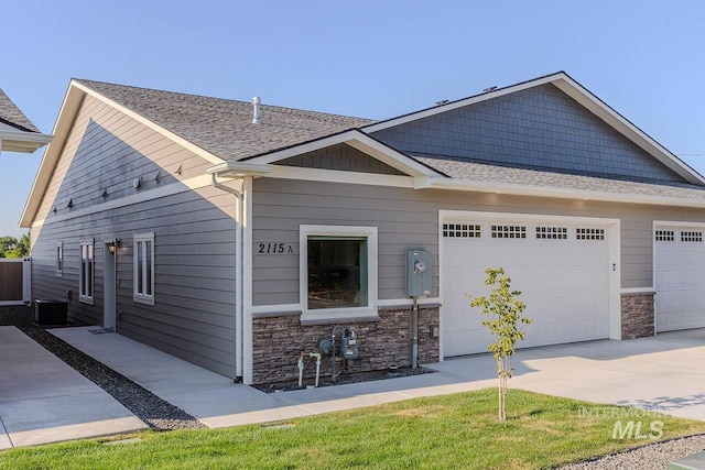 view of front of home featuring stone siding, concrete driveway, an attached garage, and cooling unit