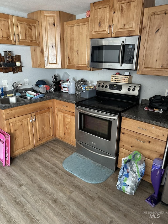 kitchen with a sink, light wood-style floors, appliances with stainless steel finishes, and dark countertops