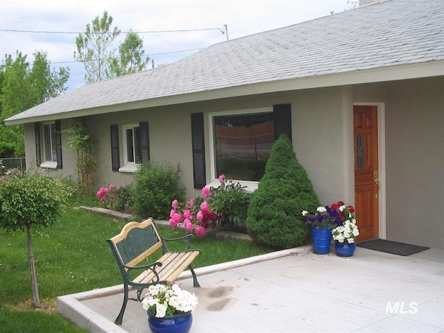 exterior space with a yard, roof with shingles, and stucco siding
