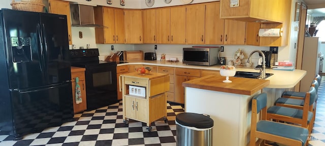 kitchen featuring sink, wooden counters, a kitchen island, wall chimney exhaust hood, and black appliances