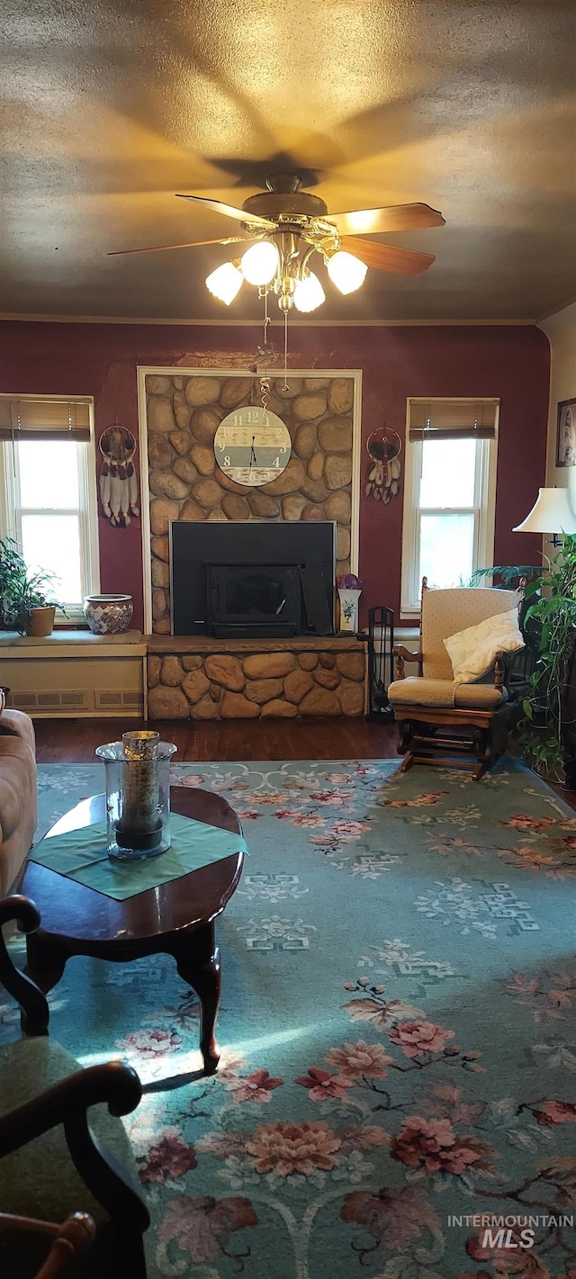 living room featuring ceiling fan, a textured ceiling, a fireplace, and a wealth of natural light